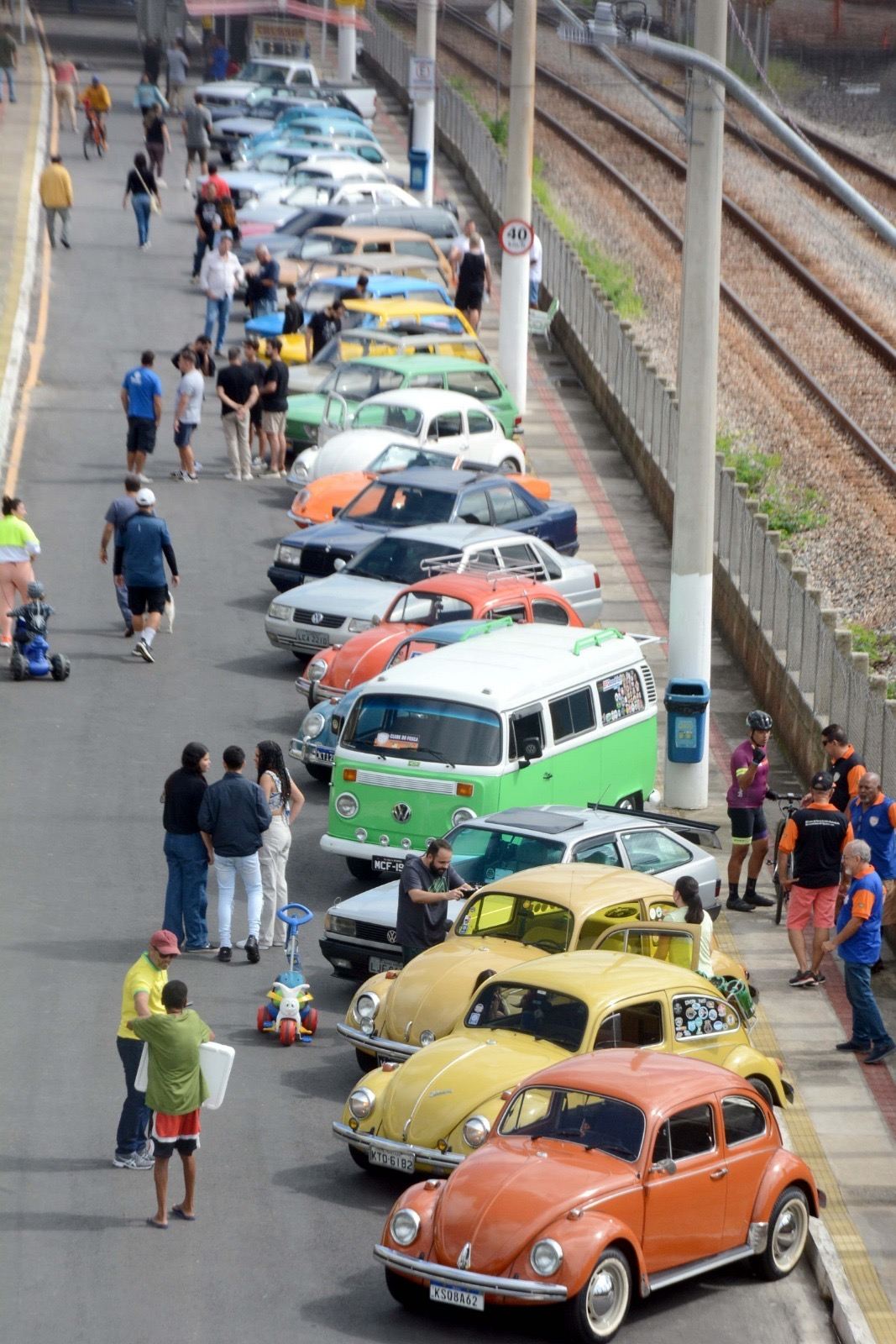 Encontro de carros antigos na Avenida Roosevelt Brasil, com fuscas e uma kombi estacionados e famílias passeando ao lado da linha do trem